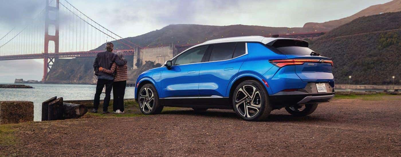 A blue 2027 Chevy Equinox EV parked by a couple overlooking a lake and bridge.