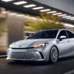 2025 Toyota Camry Hybrid driving through Lake Park FL streets showcasing modern design and hybrid efficiency