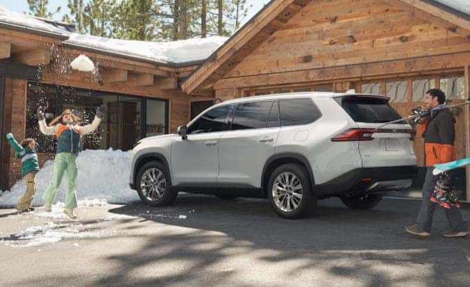Toyota Grand Highlander parked outside a cabin with a family enjoying winter activities