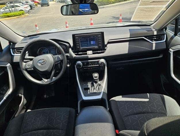 Interior view of a pre-owned Toyota RAV4 showing dashboard, steering wheel, and touchscreen display