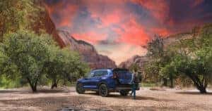 2025 Honda CR-V Hybrid parked at a trailhead in the desert at sunset with a person unloading their backpack into the trunk