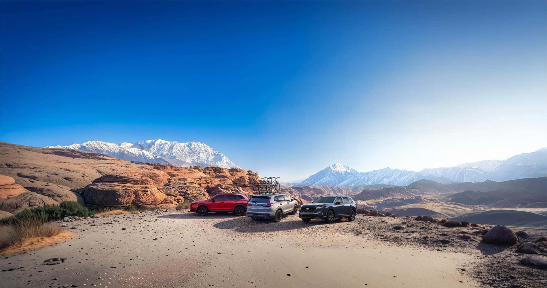 2026 Honda CR-V Hybrid Sport vs Sport L vs Touring parked on a desert overlook with snow capped rocky mountains in the distance