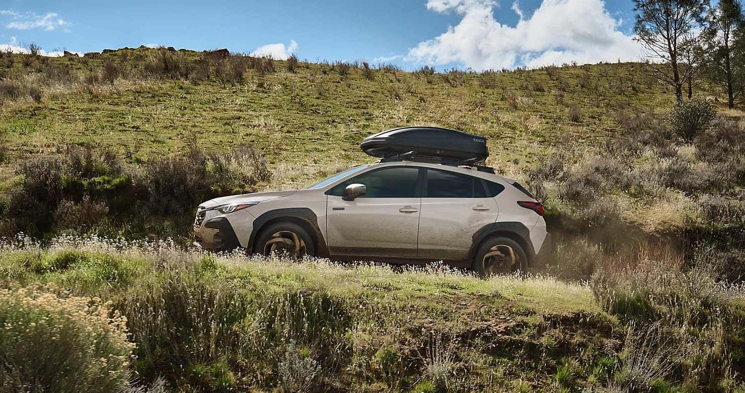 2026 Subaru Crosstrek driving on a dirt trail with a roof cargo box, highlighting off-road capability and rugged outdoor versatility