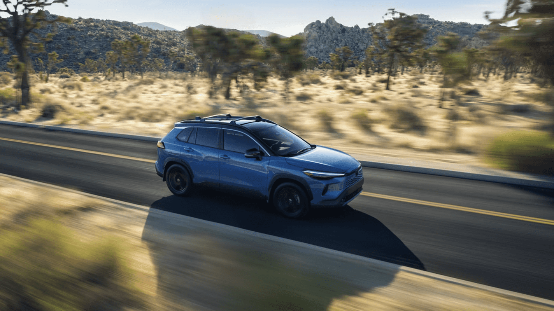 2026 Toyota Corolla Cross driving on an open highway through a dry landscape, highlighting fuel efficiency and everyday commuting capability