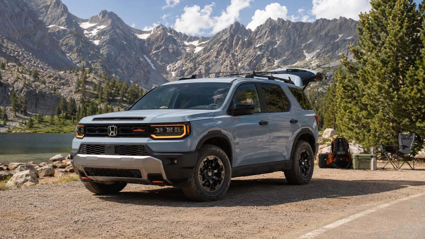 2026 Honda Passport TrailSport parked beside a mountain lake with camping gear and rocky peaks in the background.