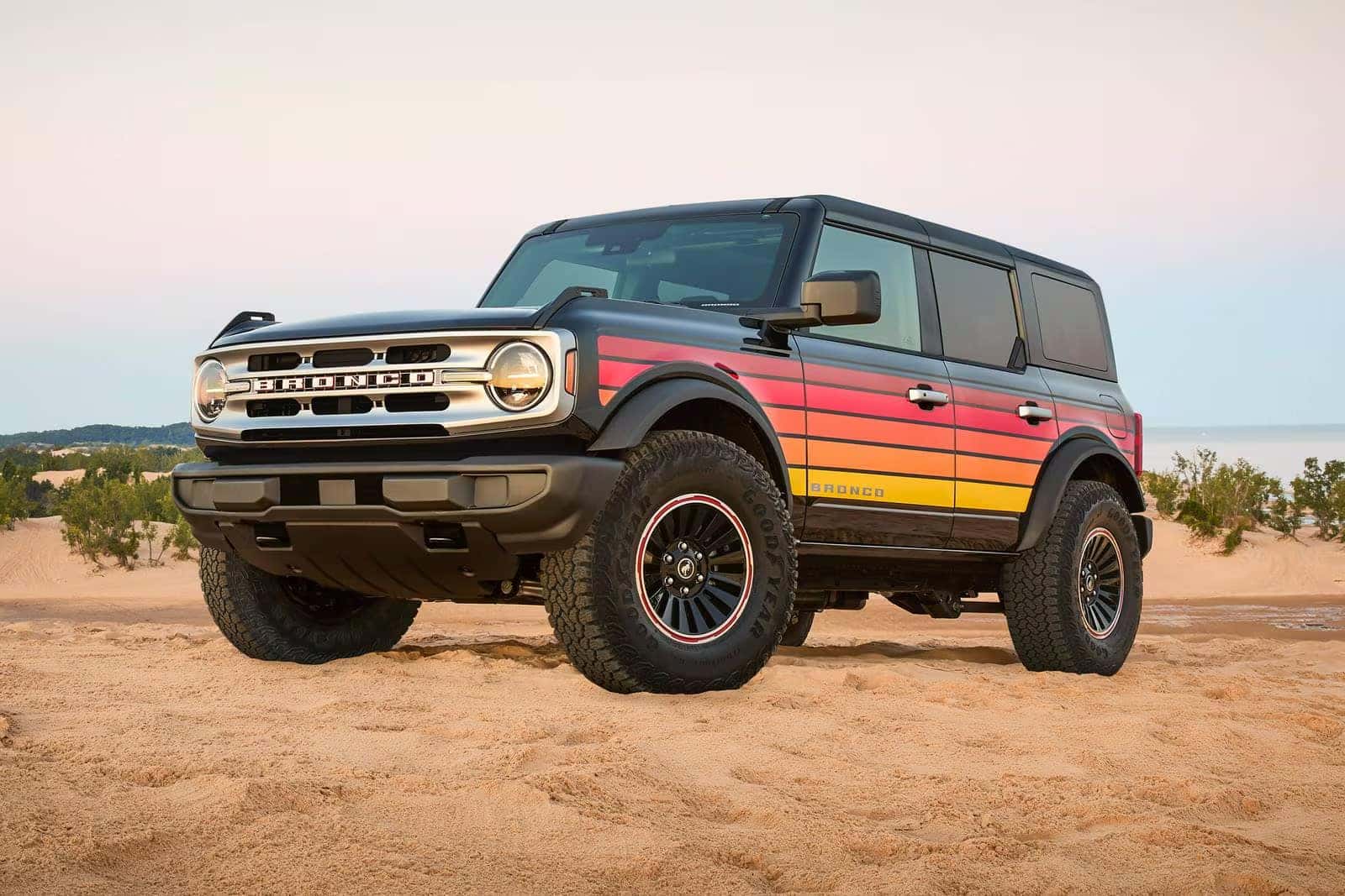 Black Ford Bronco with red and orange side graphics parked on sand near coastal dunes.