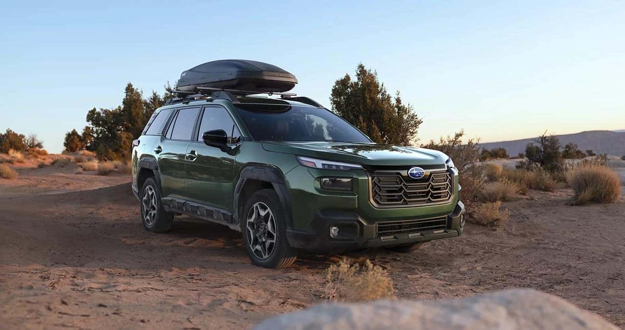 Green Subaru Outback Wilderness with a roof cargo box parked on a rocky desert trail.