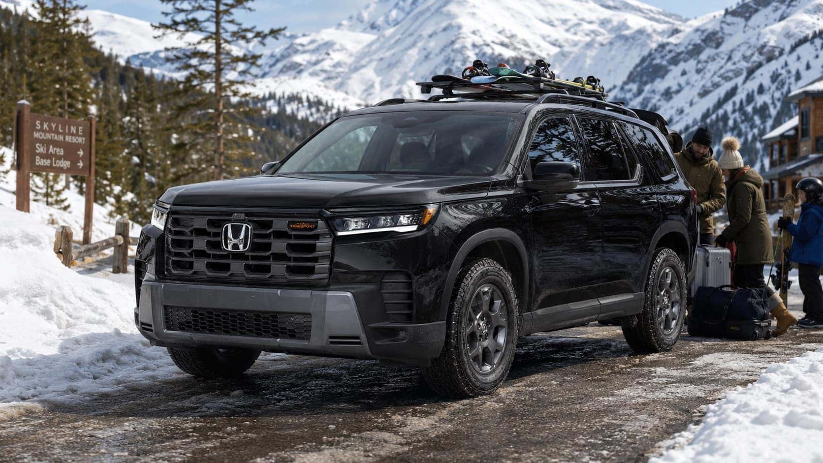 Black 2026 Honda Pilot TrailSport driving on a snowy mountain-access road with ski gear and family travel bags, showing rugged three-row SUV capability in a winter setting.