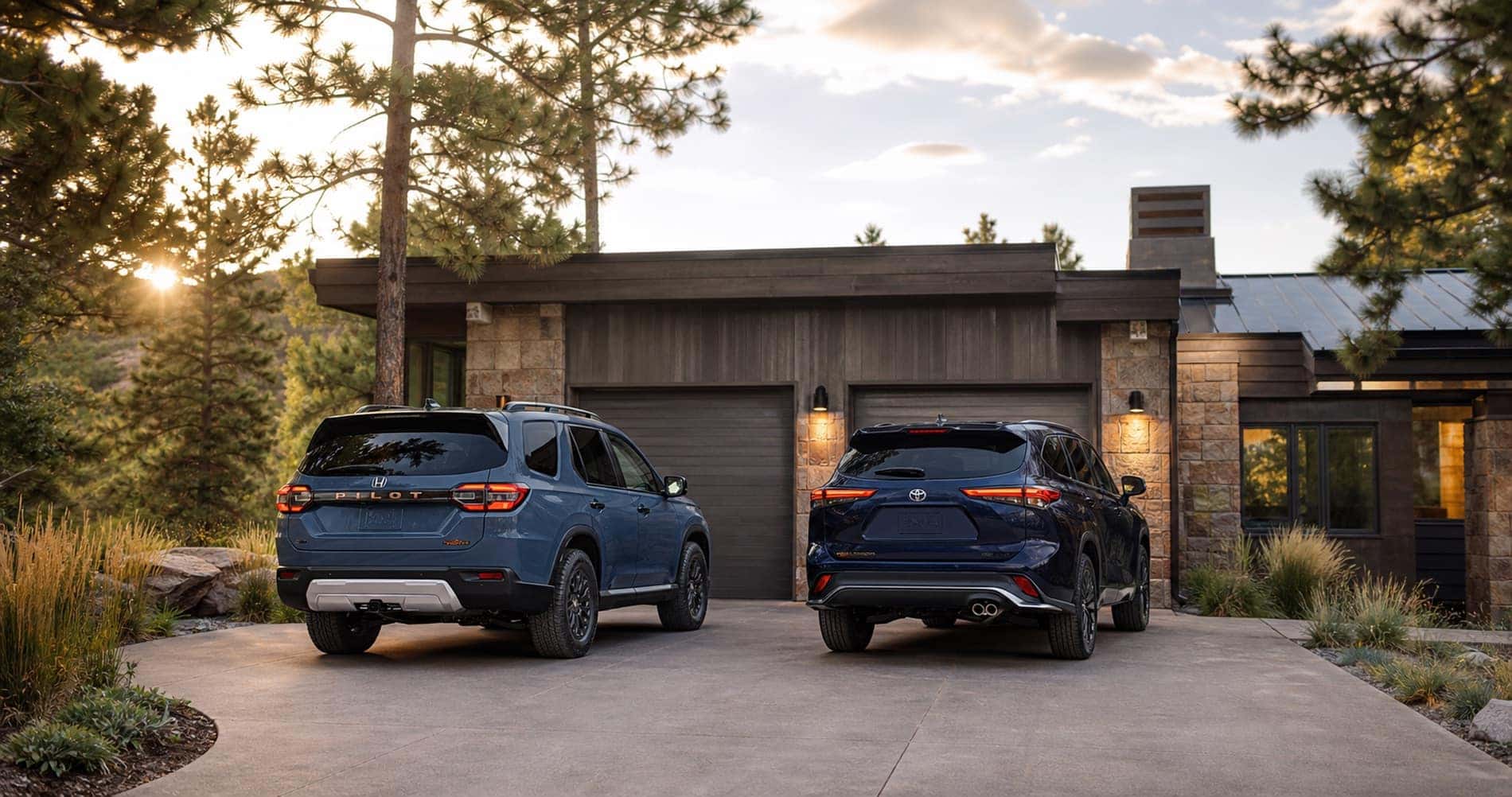 Blue Honda Pilot and blue Toyota Highlander parked side by side in driveway at sunset in front of modern mountain home highlighting rear styling and design differences.