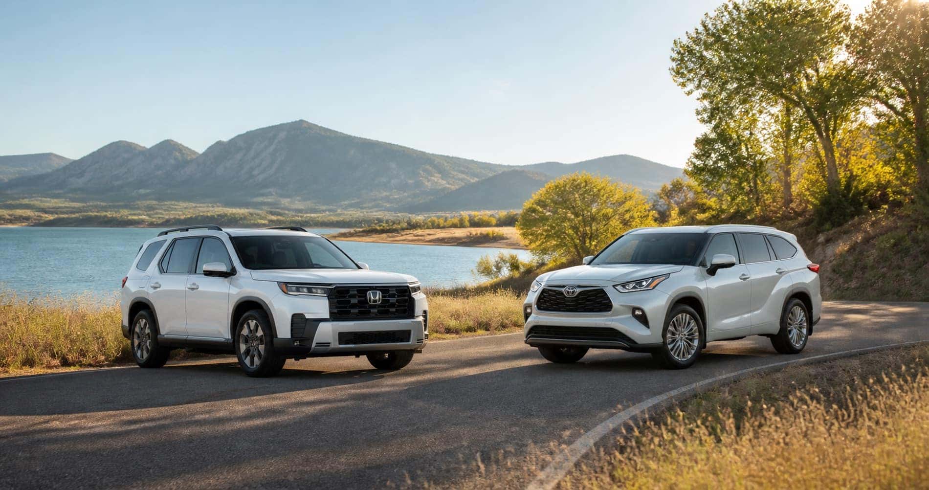 White Honda Pilot and white Toyota Highlander parked near lake with mountain scenery in background highlighting SUV proportions and outdoor versatility.