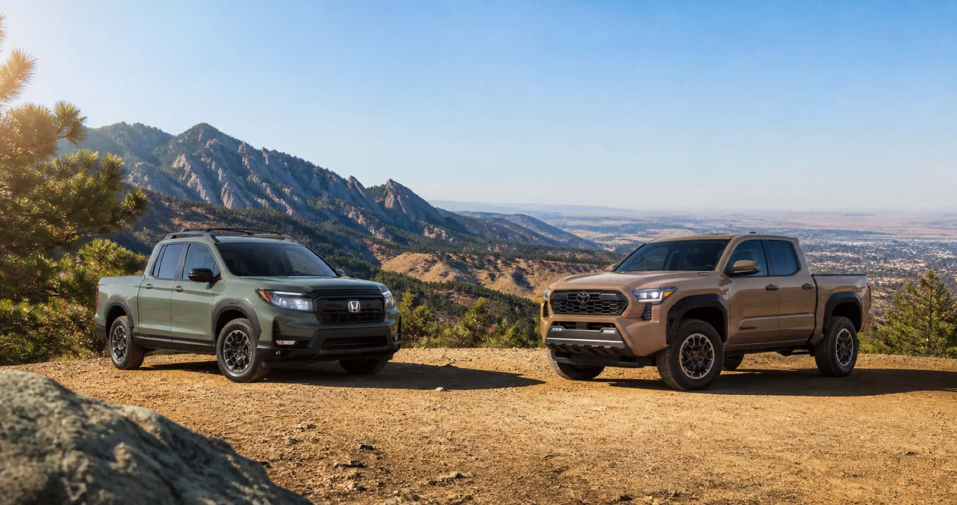 Green Honda Ridgeline and tan Toyota Tacoma parked on dirt overlook with mountain backdrop under clear blue sky showcasing front grille designs and off road capability.