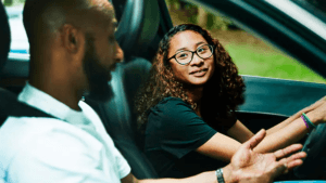 Teenaged daughter sitting in driver seat as father guides from passenger seat