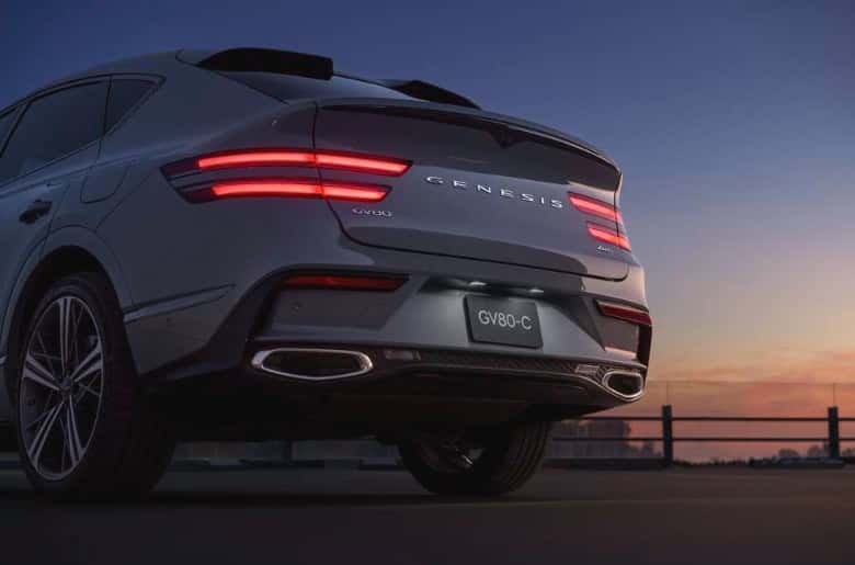 Rear view of a 2026 Genesis GV80 Coupe at dusk showing its full-width taillights, rear spoiler and dual exhaust outlets, at Genesis of North Cincinnati.