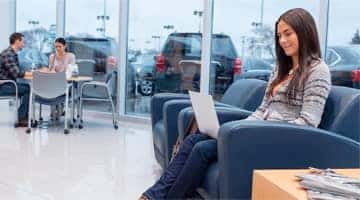 A girl sitting inside a dealership, looking at her computer.