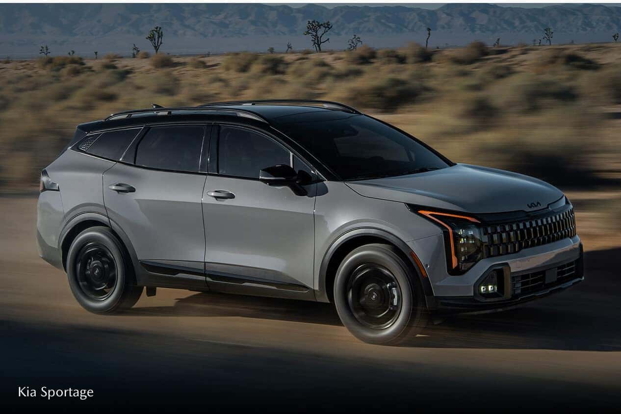 A side view action shot of a gray Kia Sportage driving down a remote desert road.