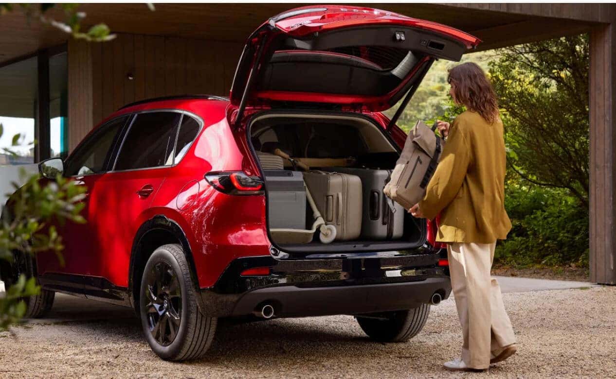 Exterior rear view of a red Mazda CX-5 with an open tailgate as a woman loads the trunk with luggage.
