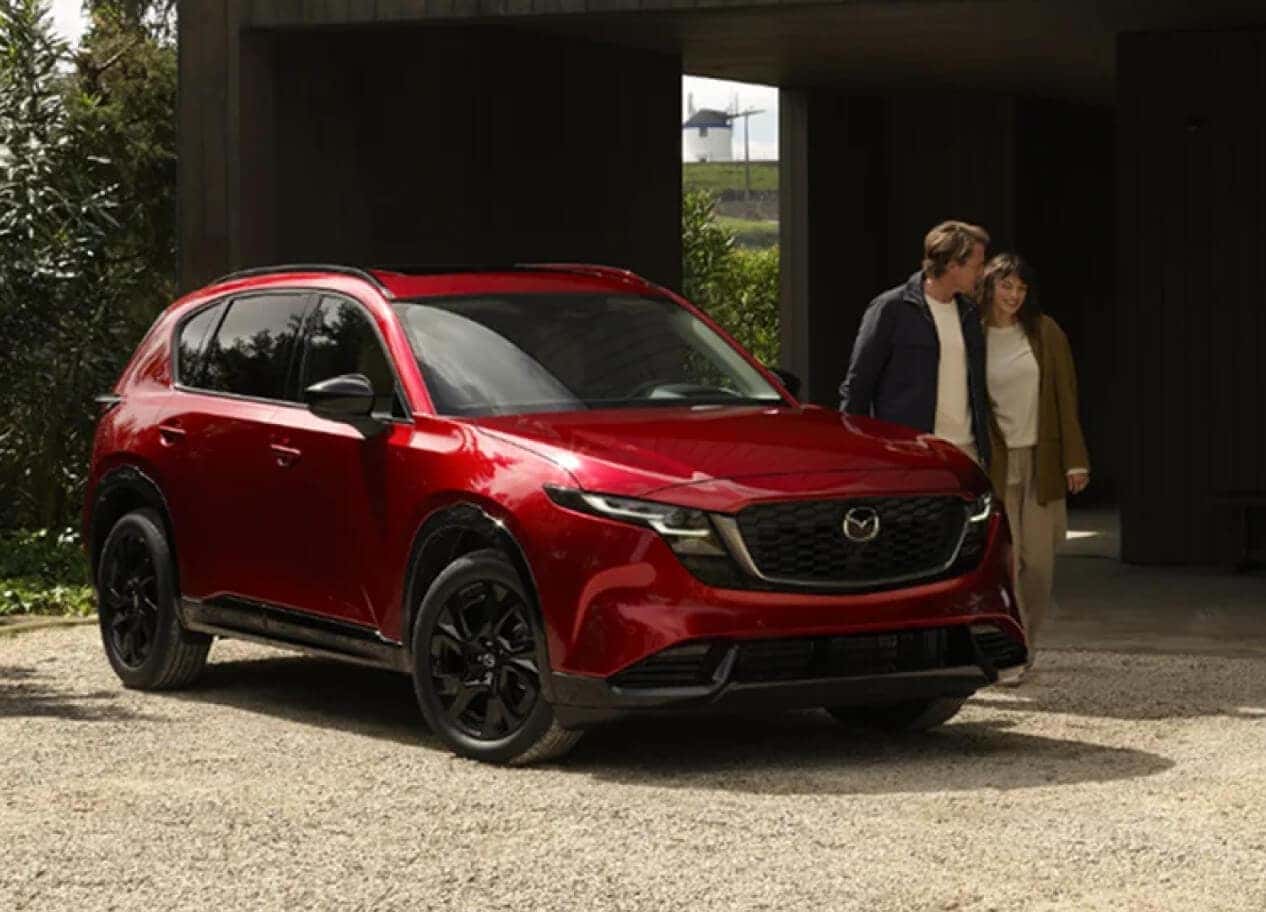 Exterior front view of a couple walking near a red Mazda CX-5 while parked in an upscale driveway.
