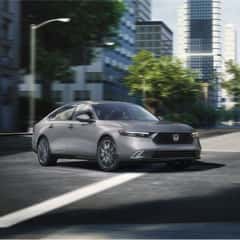 A side facing silver Accord Hybrid driving in the city