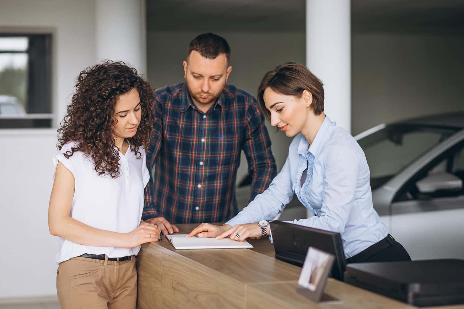 Lancaster Toyota is a Toyota Dealer Near Lancaster PA | Financial Advisor Signing Papers with Young Couple Gray Car in Backgrouund