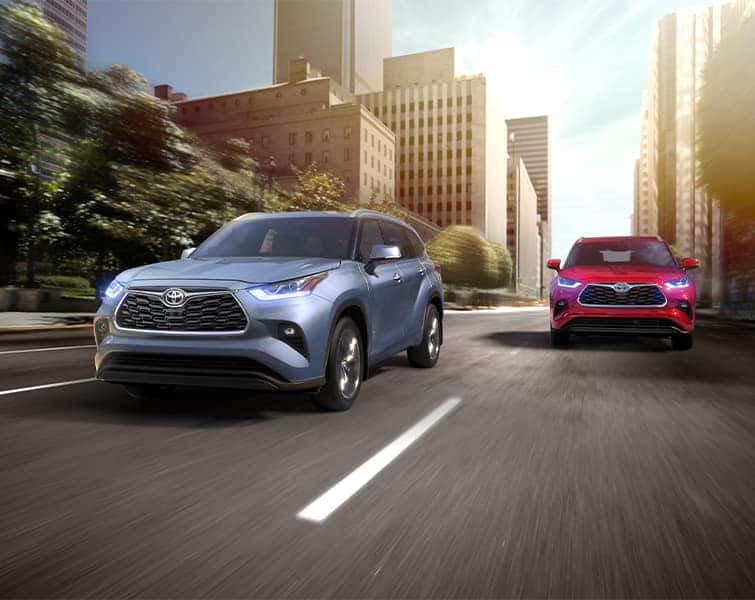 Blue 2020 Highlander and Red 2020 Highlander Hybrid Driving Through City