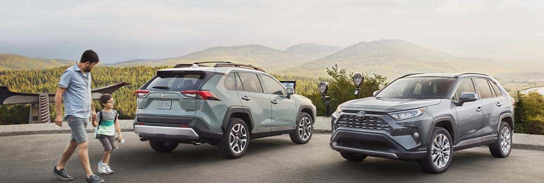 Compare the 2021 Toyota RAV4 vs. the 2021 Nissan Rogue at Lancaster Toyota | Adult and child walk to two RAV4s