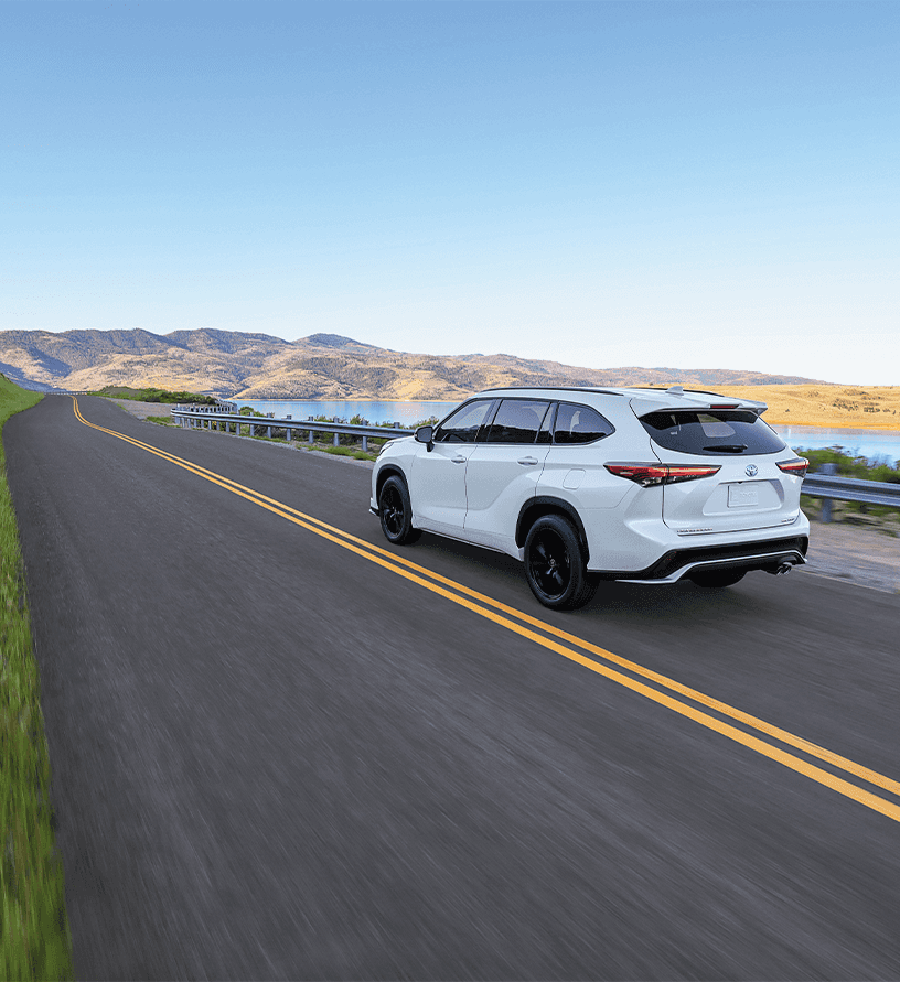 2023 Toyota Highlander at Lancaster Toyota in East Petersburg, PA | Rear view of a white 2023 Toyota Highlander driving down empty road with mountains in the background