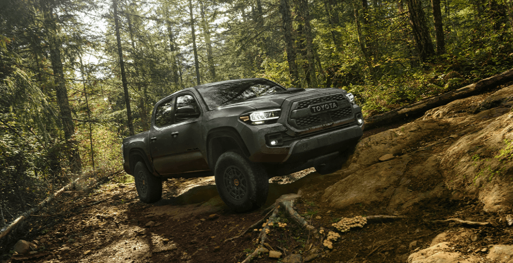 2023 Tundra vs 2023 Tacoma at Lancaster Toyota | Dark grey 2023 Toyota Tacoma driving up a dirt hill in the middle of a forrest