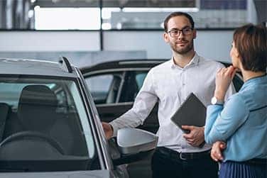 Vehicle Registration Taxes and Fees at Lancaster Toyota in East Petersburg, PA | Sales associate holding a clipboard talking to customer while showing new car inside of dealership