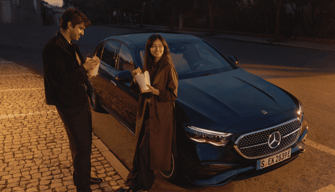 A couple stands outside a new Mercedes-Benz car parked on a city street.