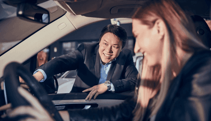 A Mercedes-Benz salesman points out interior features while she sits behind the wheel of a Mercedes car.