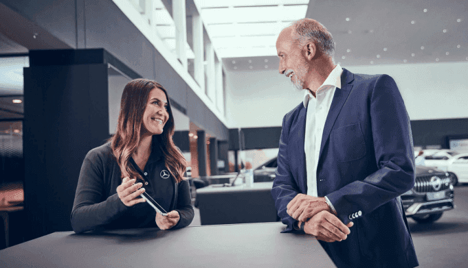 A mercedes-Benz representative holds an iPad and smiles while talking to a customer.