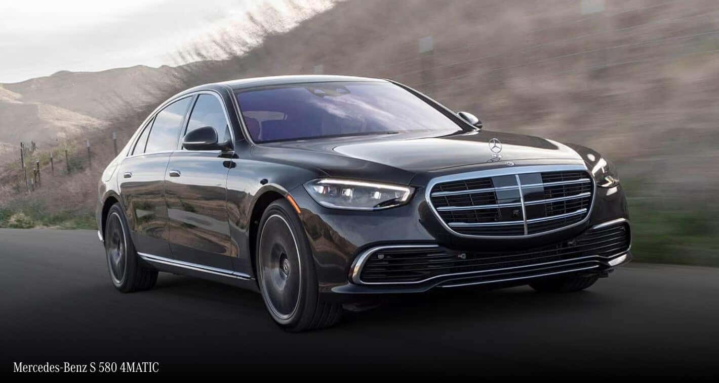 Low angle front three-quarter action shot of a black Mercedes-Benz S 580 4MATIC on a beachside road.