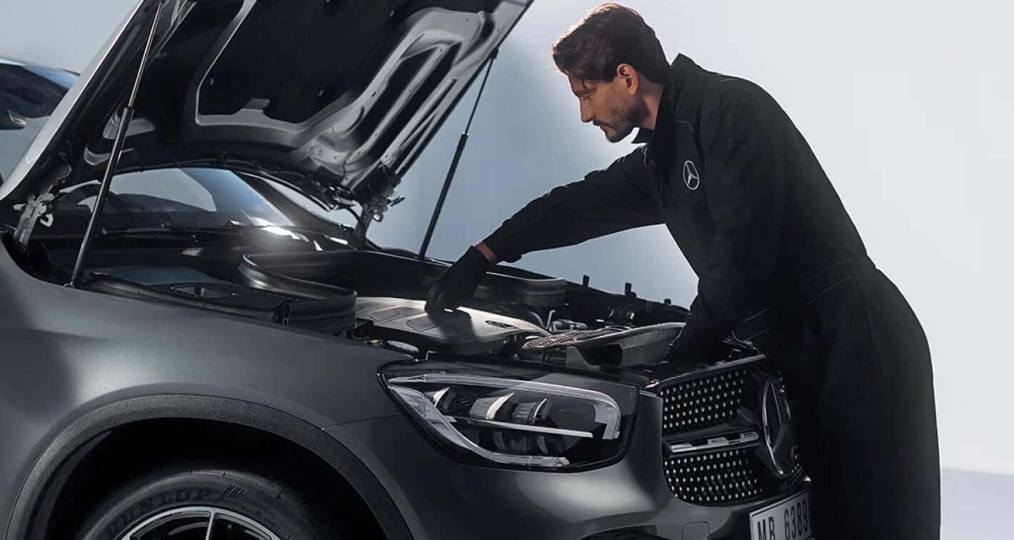 A Mercedes-Benz Certified Technician makes adjustments under the hood of a Mercedes Sedan.