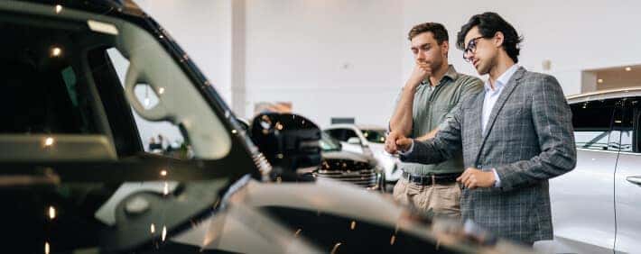 Dealership ales advisor discusses a pre-owned vehicle with a customer inside a bright luxury dealership showroom.