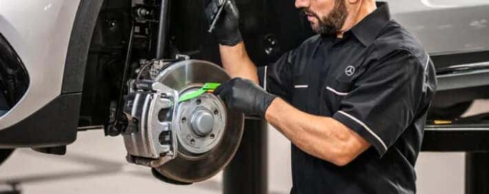 Mercedes-Benz technician inspects and services a vehicle's exposed brake rotor and caliper inside a service bay.