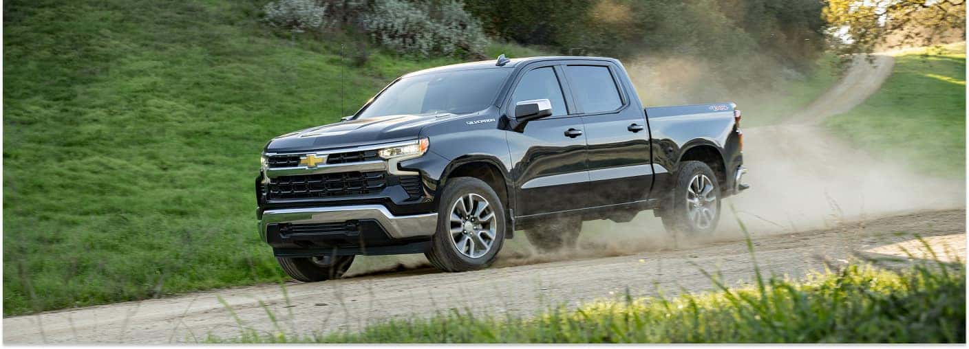 Black 2026 Chevrolet Silverado 1500 pickup truck driving on a dirt road kicking up dust.