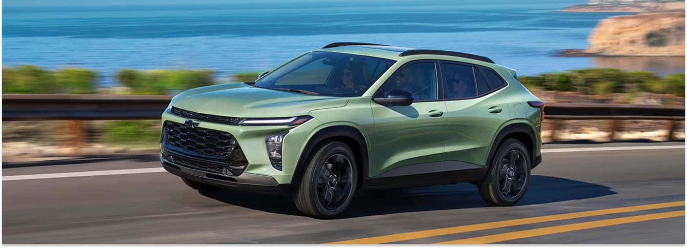 Light green 2026 Chevrolet Trax driving along a coastal highway next to the ocean.