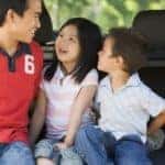 Man with two children sitting in back of van smiling
