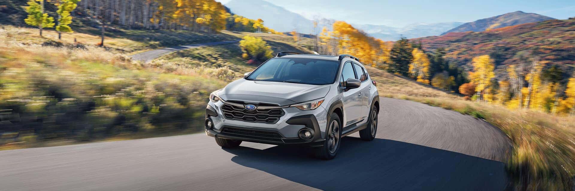 2026 silver subaru crosstrek driving down a road with mountains in the background