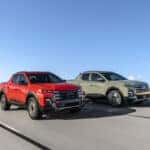 Two 2025 Hyundai Santa Cruz models, including the Santa Cruz XRT, are displayed driving on a scenic road, showcasing their rugged design.