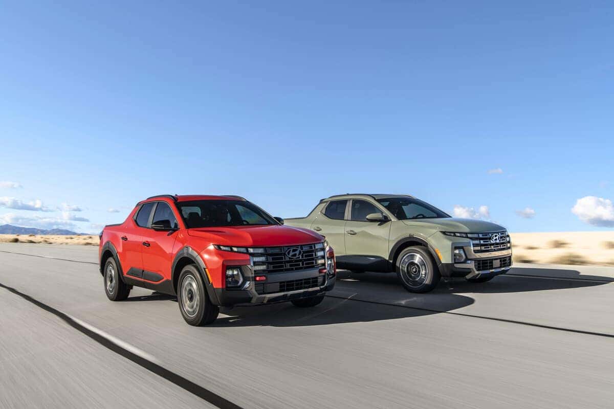 Two 2025 Hyundai Santa Cruz models, including the Santa Cruz XRT, are displayed driving on a scenic road, showcasing their rugged design.