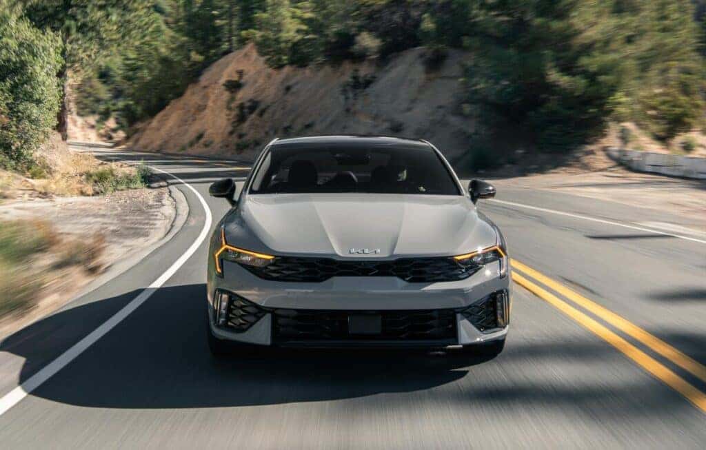 The 2025 Kia K5 drives along a scenic mountain road, highlighting its stylish exterior and adventurous spirit.
