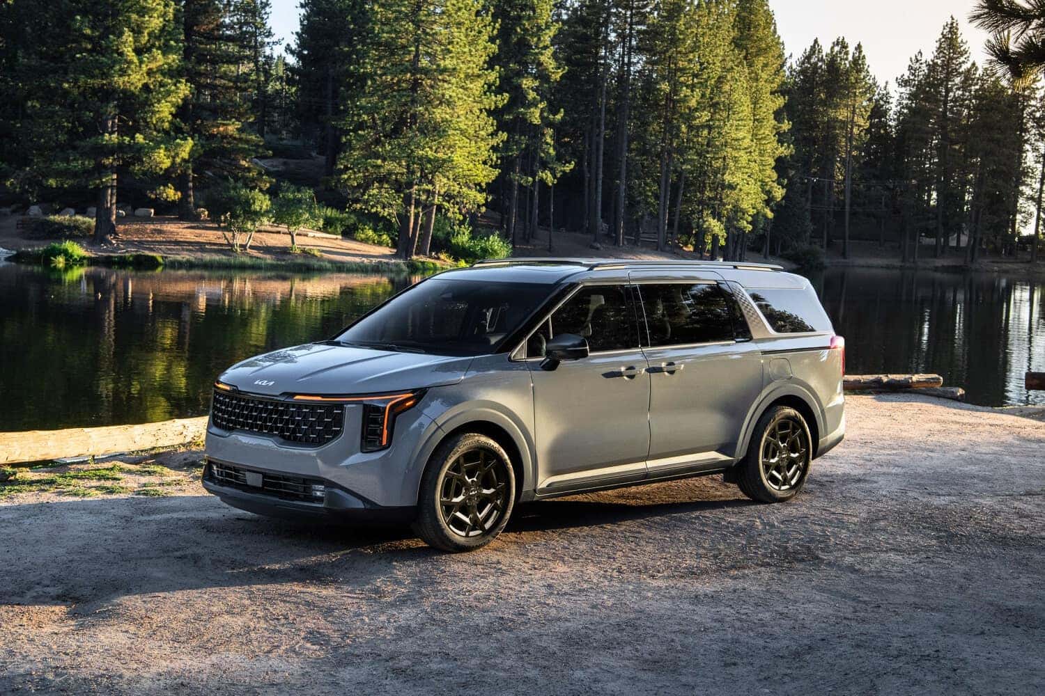 2025 KIA Carnival parked in front of a forested lake
