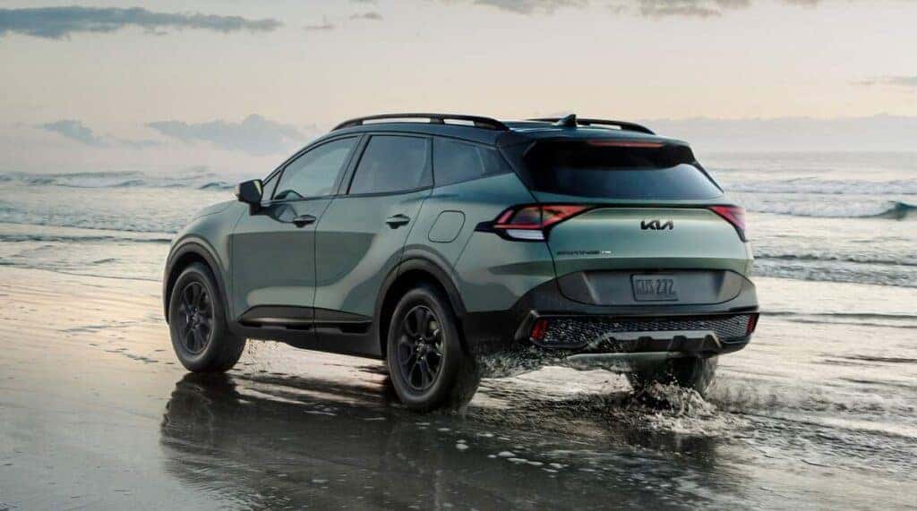 A 2025 KIA Sportage SUV driving along a sandy beach, showcasing its sleek design against a backdrop of ocean waves.