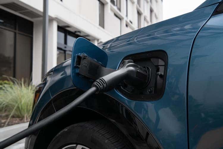 A blue 2025 KIA Niro PHEV with a charging plug connected, showcasing its eco-friendly design and technology.