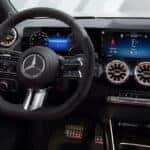 Interior of a 2026 Mercedes-Benz GLA, featuring a dual-screen digital dashboard, turbine-style air vents, and red door accents.