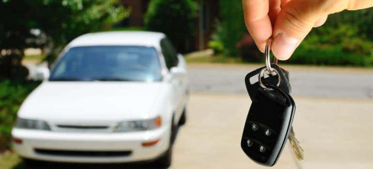 Fingers holding car keys with white car in background