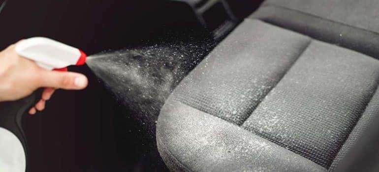 Car care concept, detailing and cleaning car interiors. Worker spraying cleaning solution on car upholstery